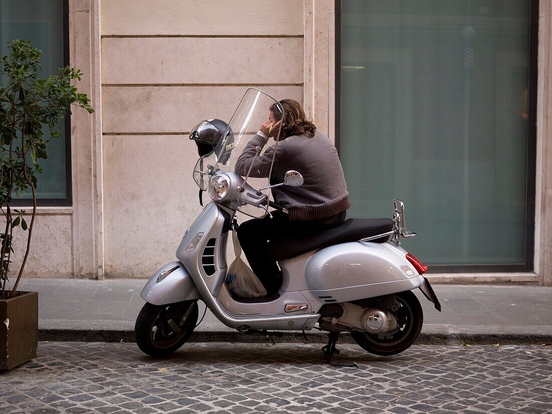 Mann am Telefon im Roller sitzend; Rom, Italien