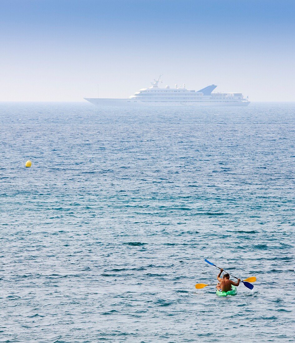 Men In Canoe And Large Yacht In Distance; Marbella, Costa Del Sol, Malaga Province, Spain