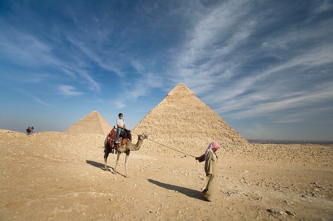 Ein Führer führt ein Kamel und einen Passagier zu den Pyramiden