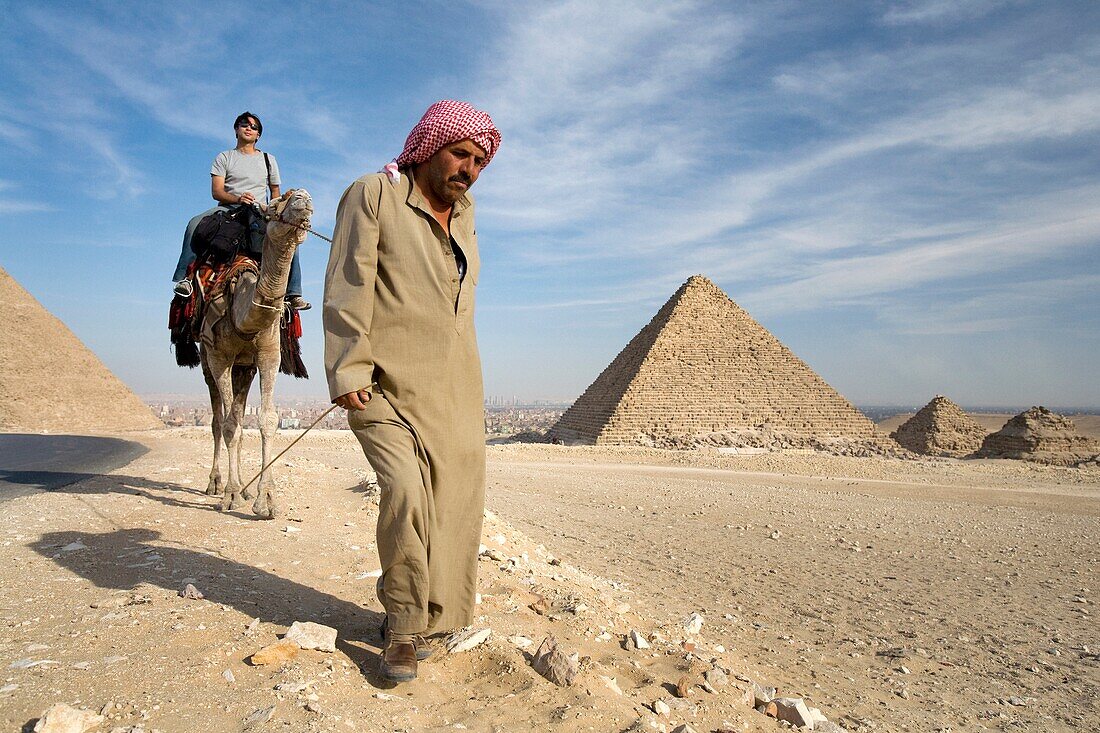 Ein Führer, der ein Kamel und einen Reisenden bei den Pyramiden führt; Kairo,Ägypten,Afrika