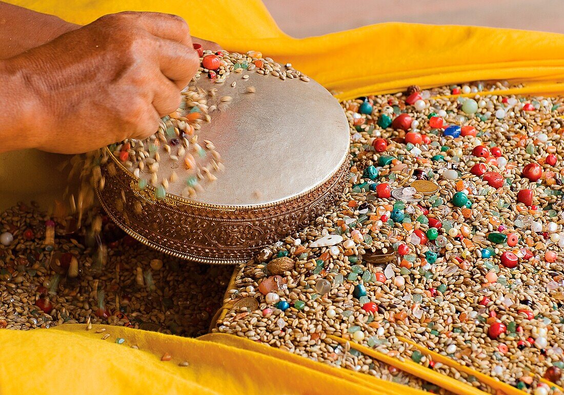 Buddhistischer Mönch lässt bunte Samen und Perlen auf eine kleine Trommel fallen; Kathmandu, Nepal
