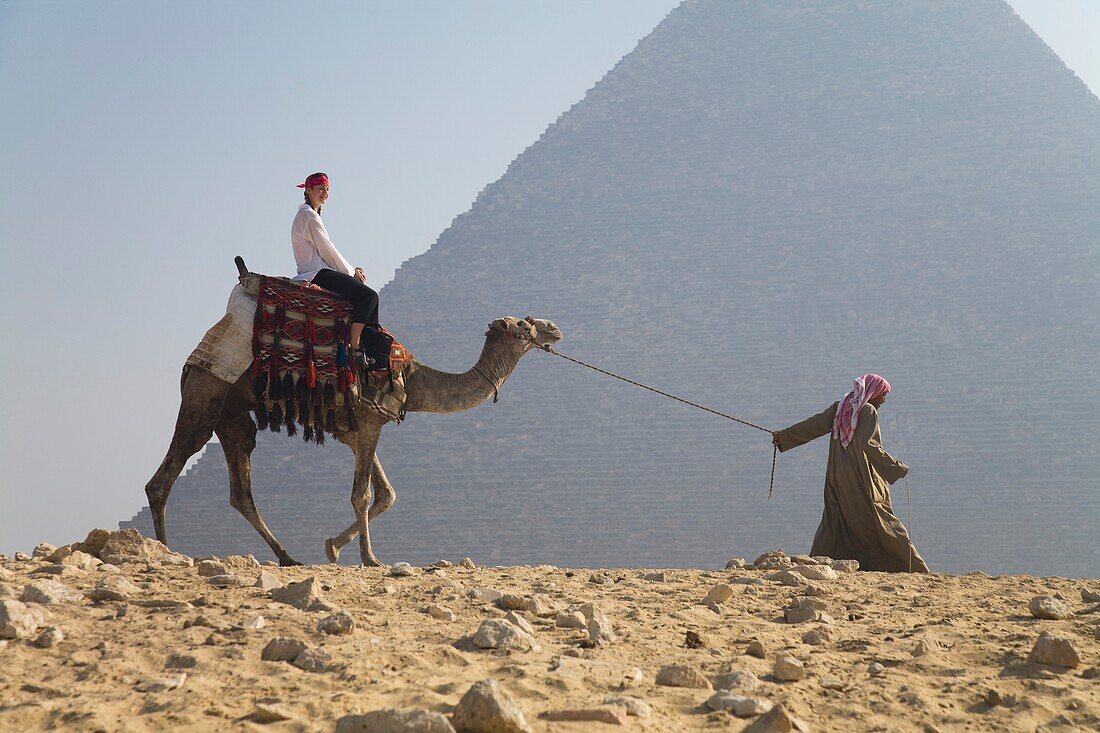 Junge Touristin auf einem Kamel, geführt von einem Führer, bei den Pyramiden von Gizeh, Ägypten