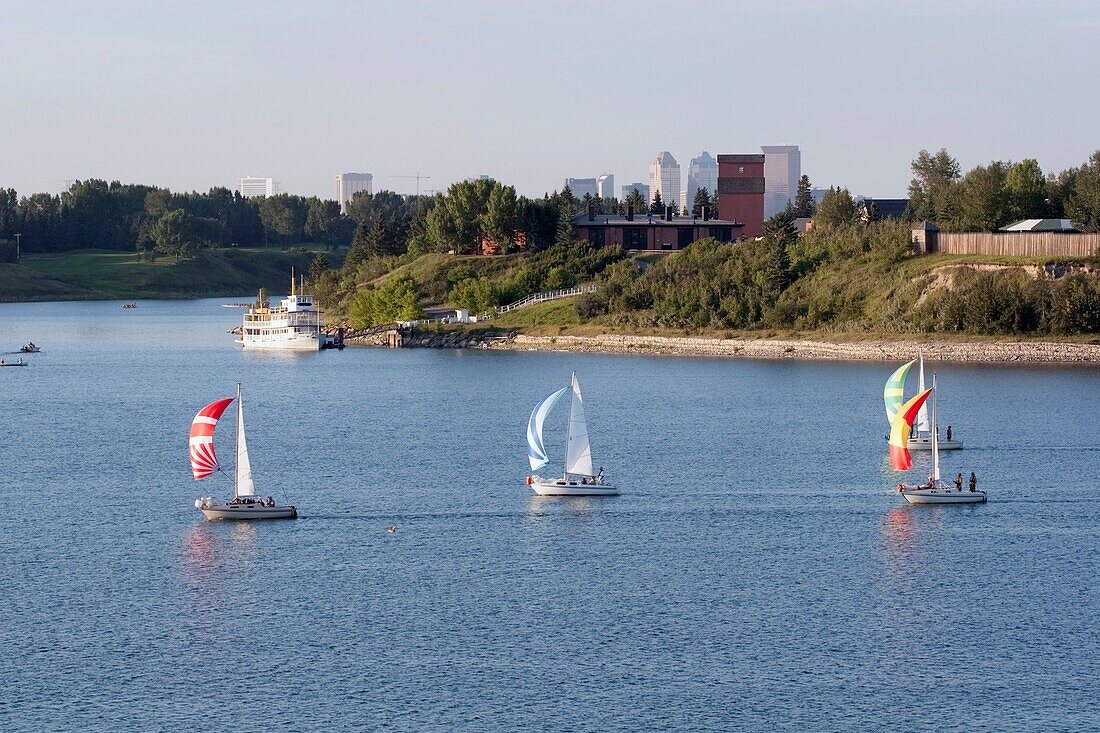 Calgary, Alberta, Kanada; Segelboote auf dem Wasser mit Heritage Park und der Stadt im Hintergrund