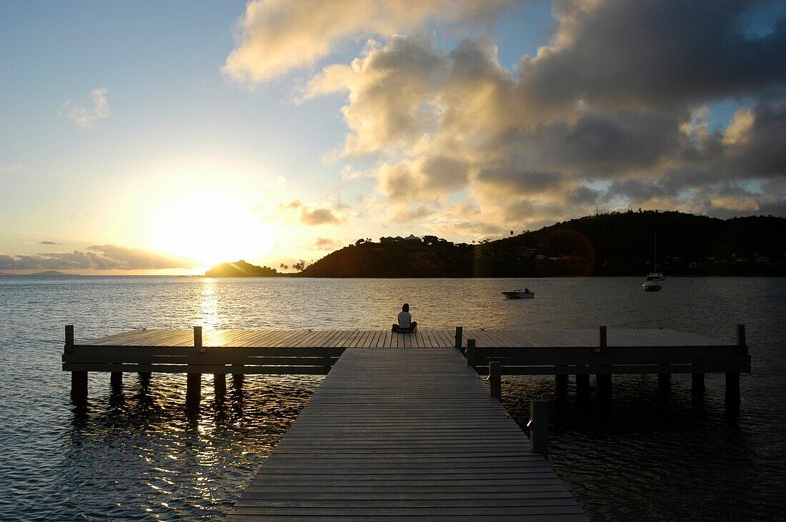 Woman Sitting On End Of Pier At Dusk