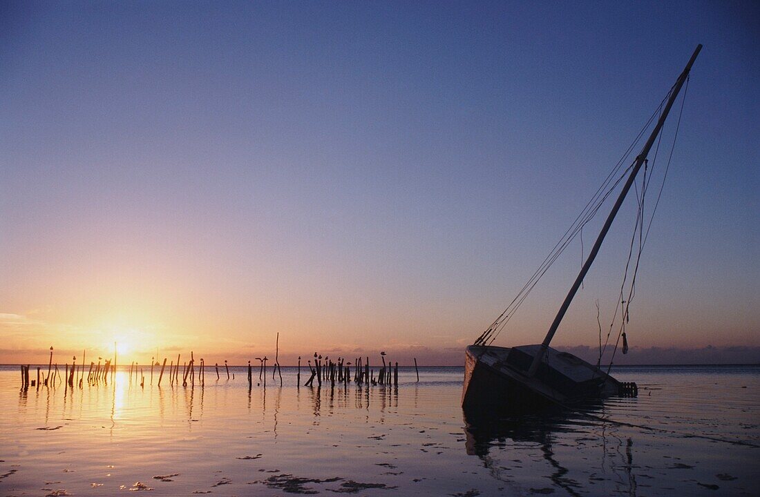 Partly Submerged And Keeling Sail Boat In Silhouette At Sunset
