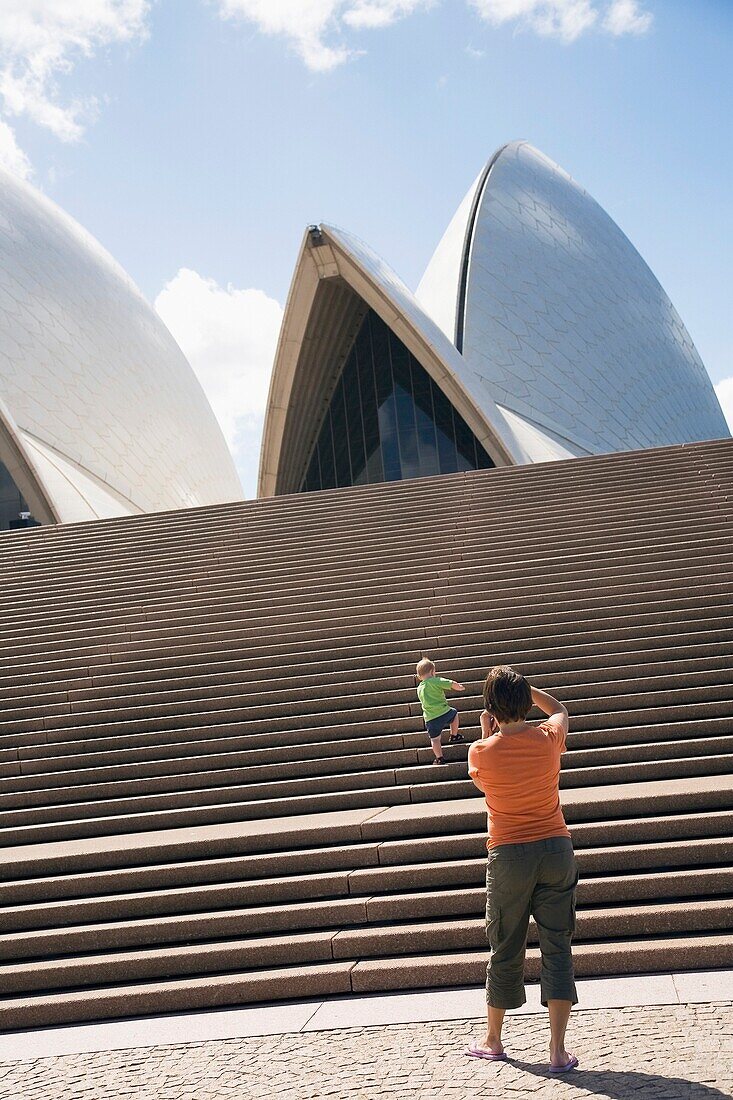 Mutter fotografiert ihren Sohn, der die Treppe vor dem Opernhaus in Sydney hinaufsteigt