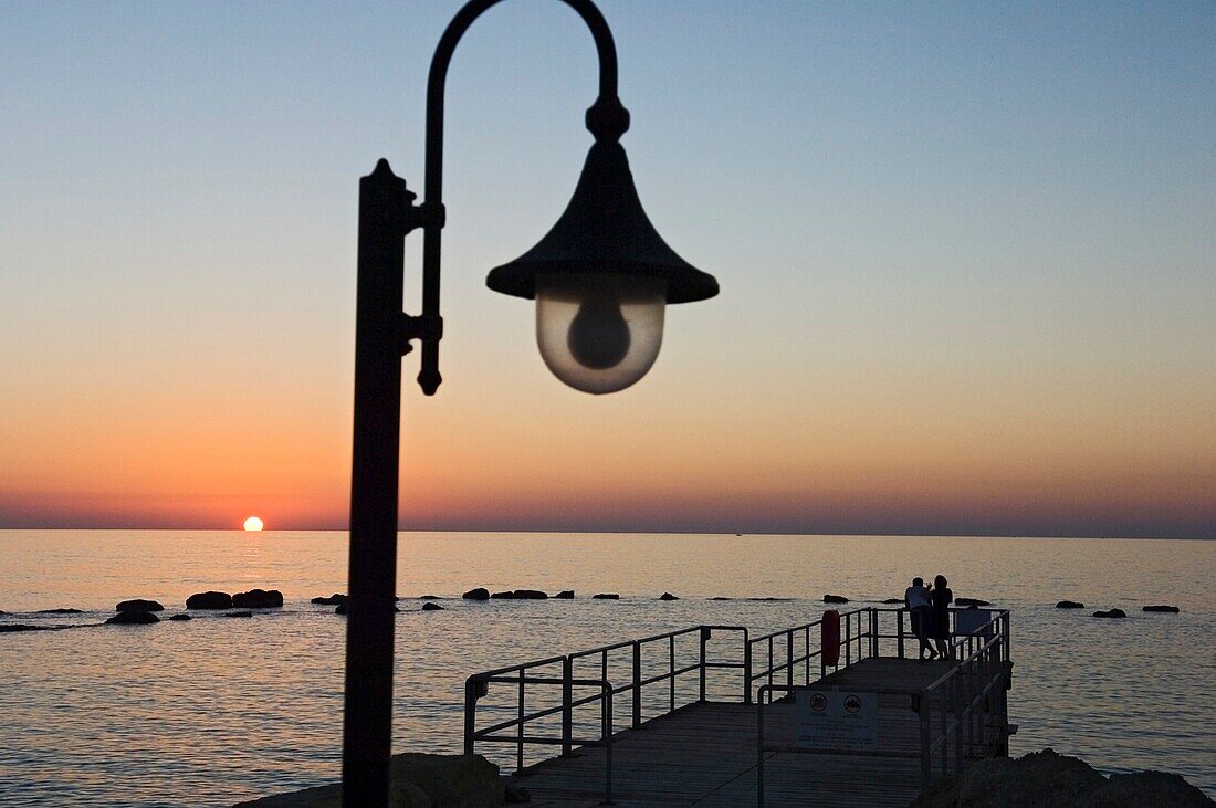 Ein Paar auf einem kleinen Pier beobachtet den Sonnenuntergang am Meer