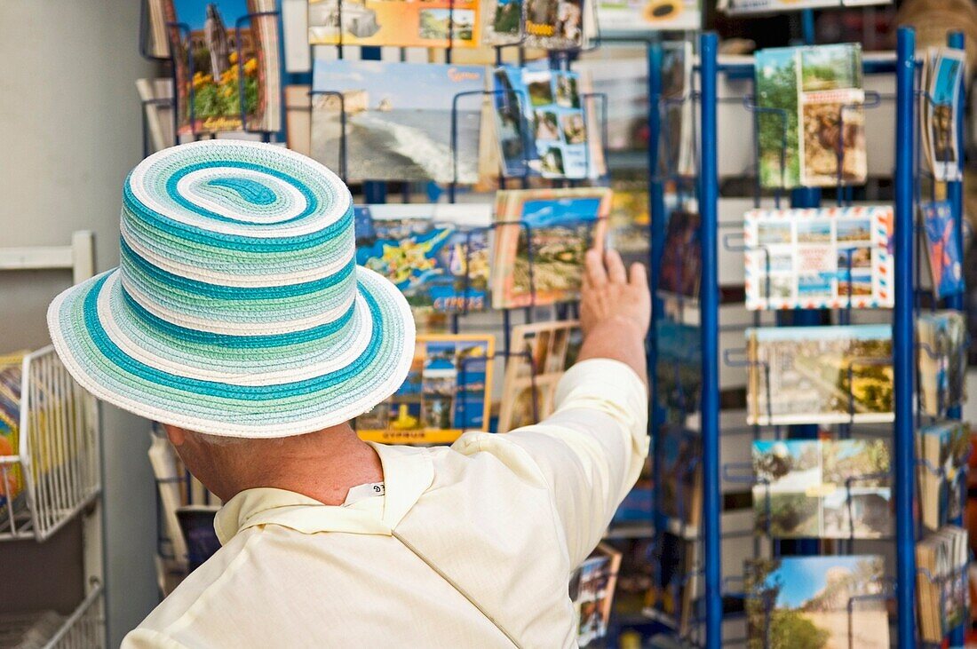 Eine Touristin mit einem bunten Hut betrachtet eine Postkarte