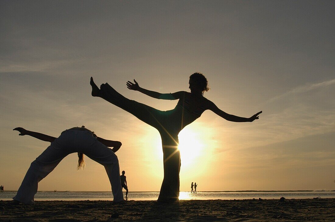 Two Women Silhouetted Doing Capoeira On Beach At Sunset