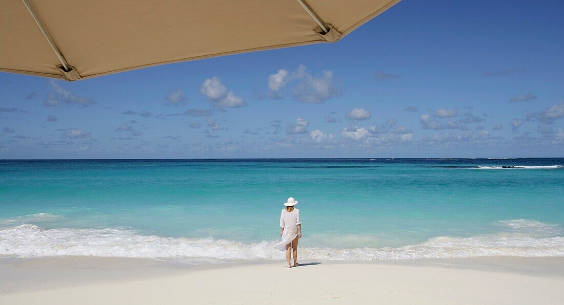 Frau steht an einem tropischen Strand mit Sonnenschirm im Vordergrund