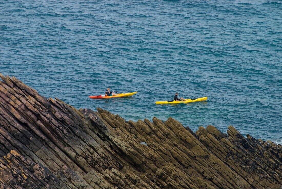Ein Paar fährt mit dem Seekajak an Felsen vorbei in der Nähe von Erquy