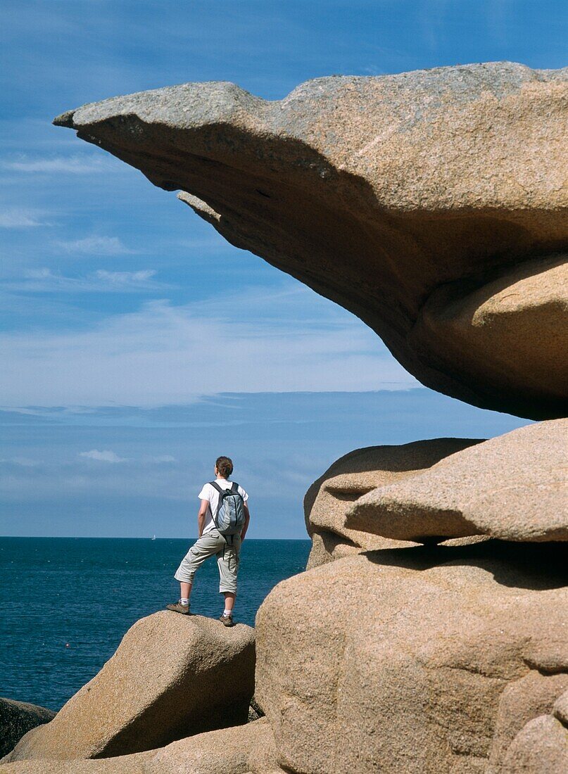 Spaziergängerin neben einer Felsformation am Meer stehend
