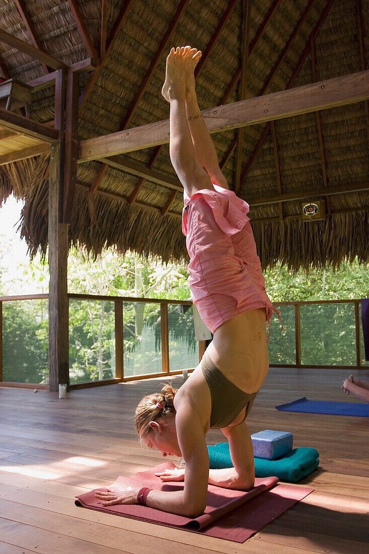 Woman Doing Hand Stand In Grass Roofed Eco Lodge