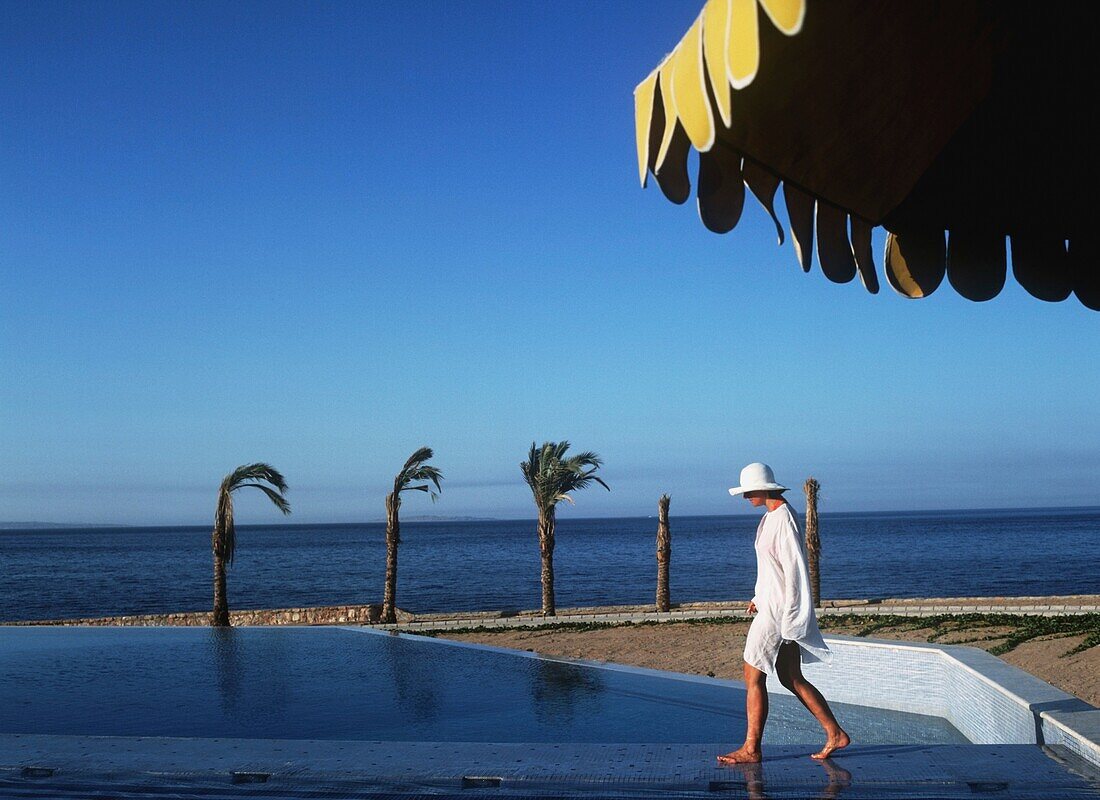 Frau mit Sonnenhut und Kaftan beim Aufwachen am Strand des Oberoi Sahl Hasheesh Resort