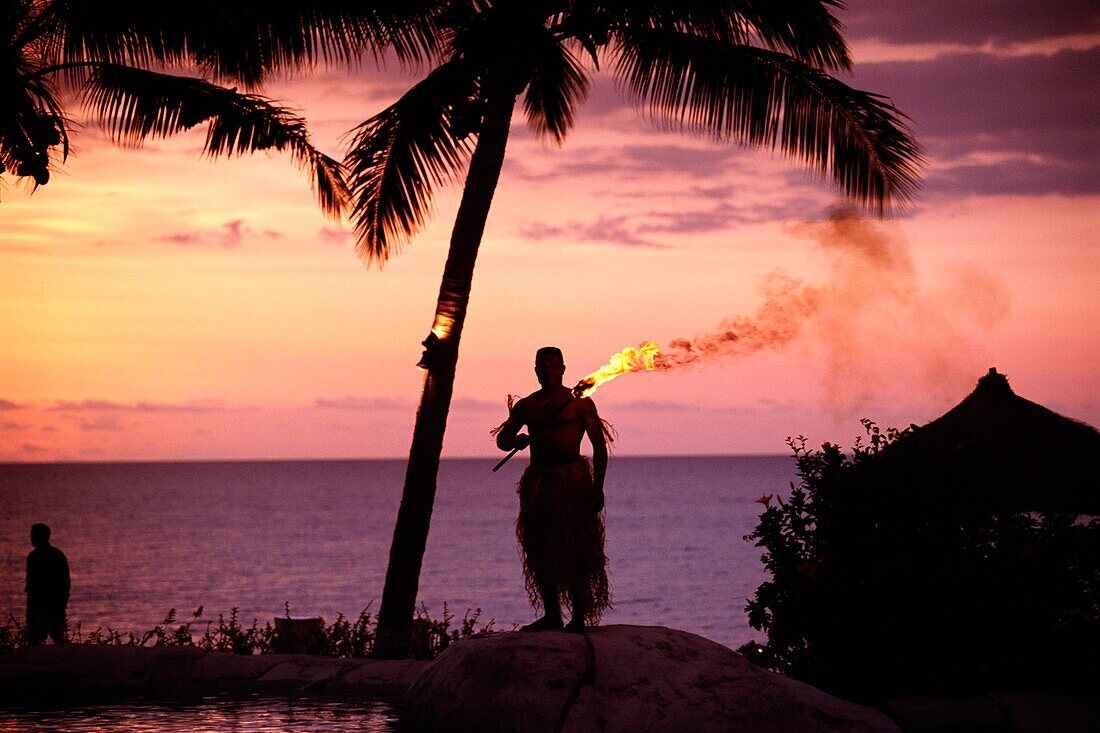 Einheimische im Grasrock hält eine brennende Fackel an der Küste bei Sonnenuntergang