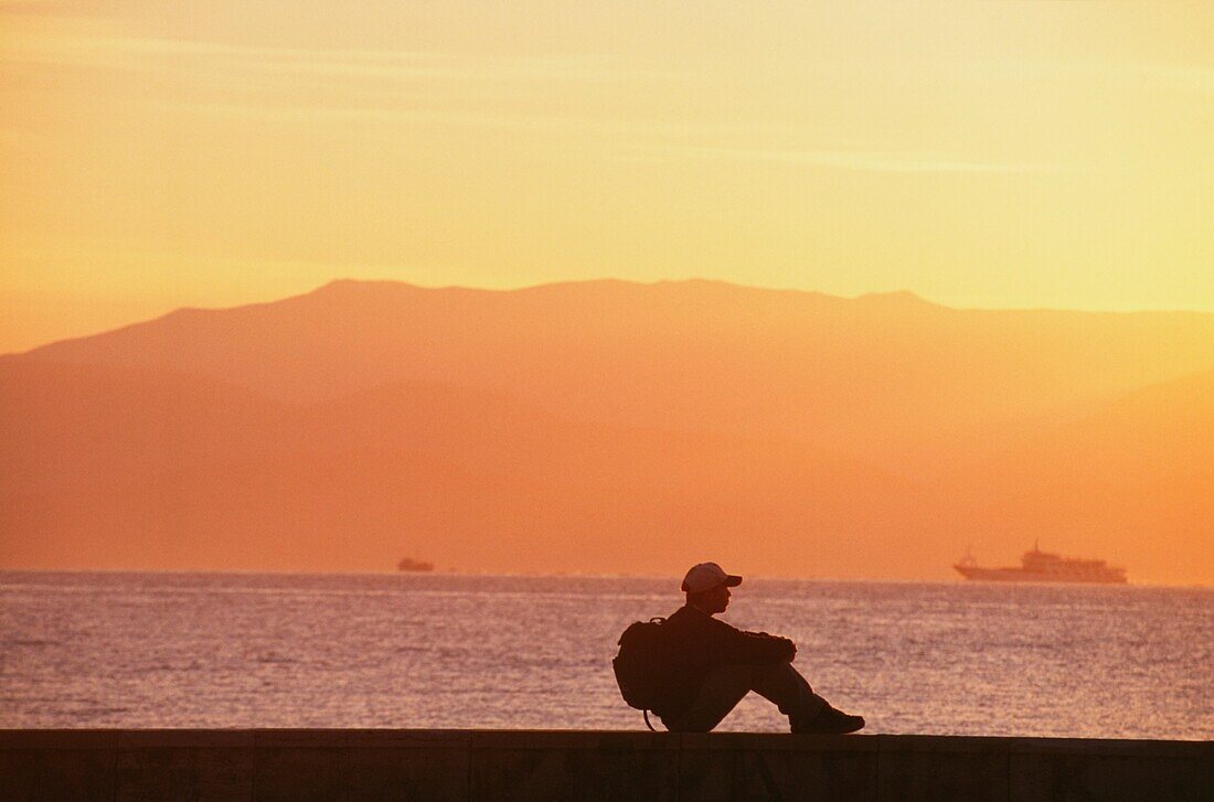 Rucksacktourist in Silhouette an der Küste sitzend