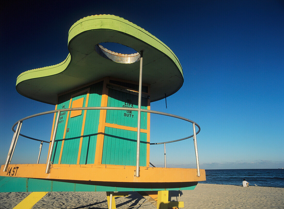 Man Sitting On Beach In The Evening In Front Of Life Guard Tower