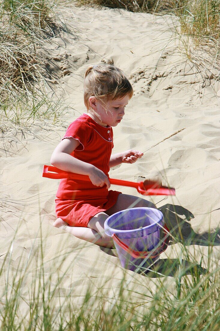 Girl Playing With Bucket And Spade On Sand Dune