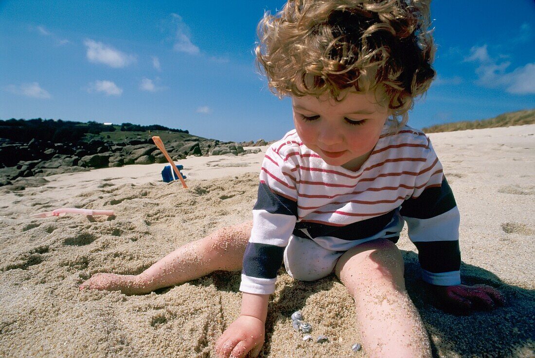 3 Jahre altes Mädchen, das am Strand der Scilly-Inseln im Sand spielt