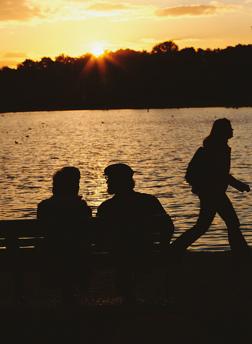 Paar auf Bank mit junger Frau im Vorbeigehen, The Serpentine, Hyde Park