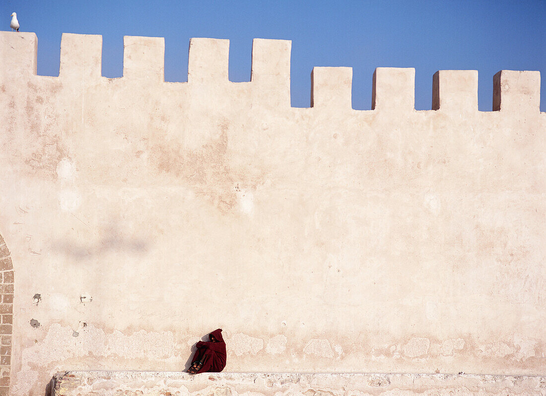 Man In The Traditional Djelleba Sitting Under The Fortified Walls