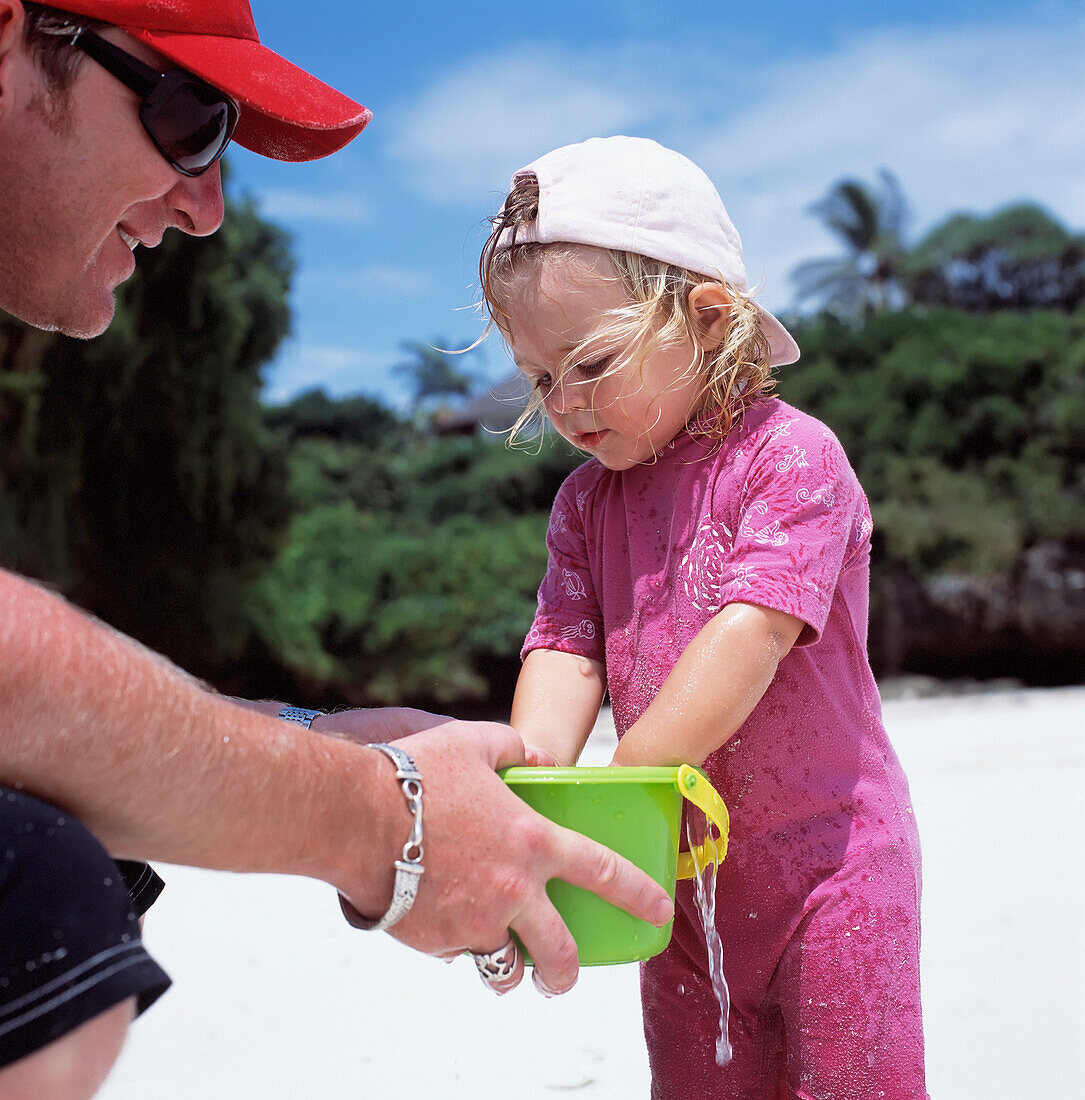 Vater hält Eimer für Tochter beim Spielen am Strand