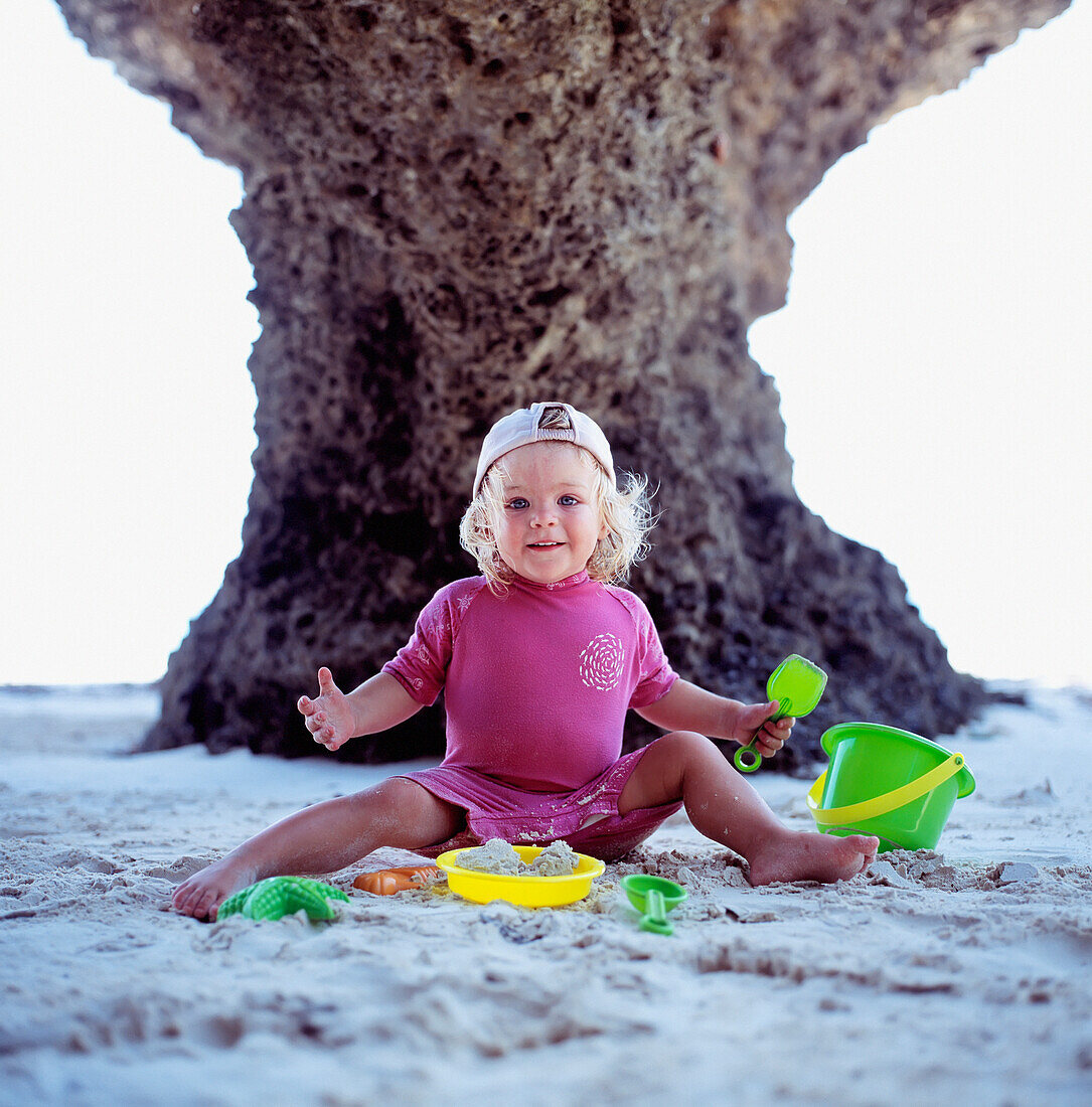 Lächelndes Mädchen, das am Strand mit Eimern und Spaten spielt