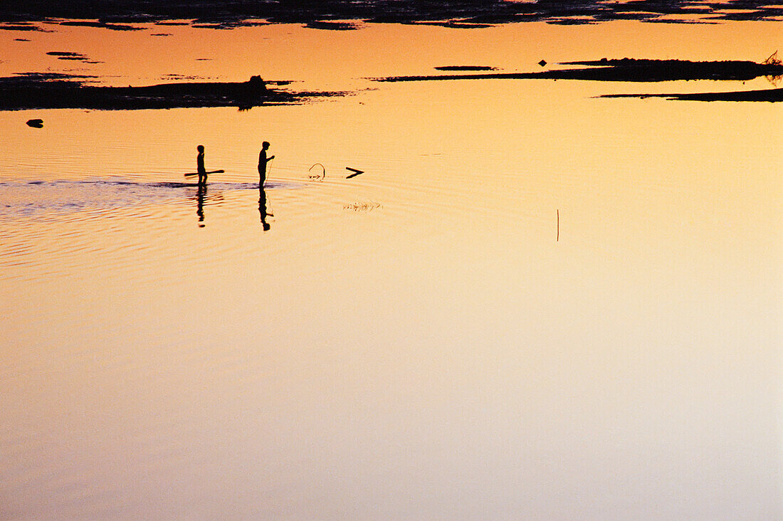 Zwei Jungen gehen bei Sonnenuntergang am Mekong-Ufer entlang