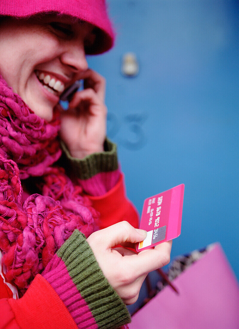 Lächelnde Frau in Rosa hält Kreditkarte und spricht mit dem Handy