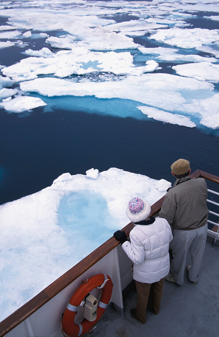 Two Tourists Looking Over Boat Railing At Floating Ice