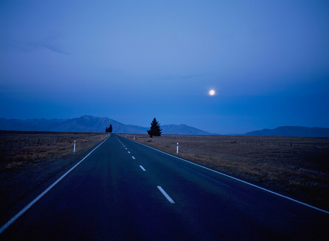 Leere Straße durch die Landschaft bei Nacht mit Mond
