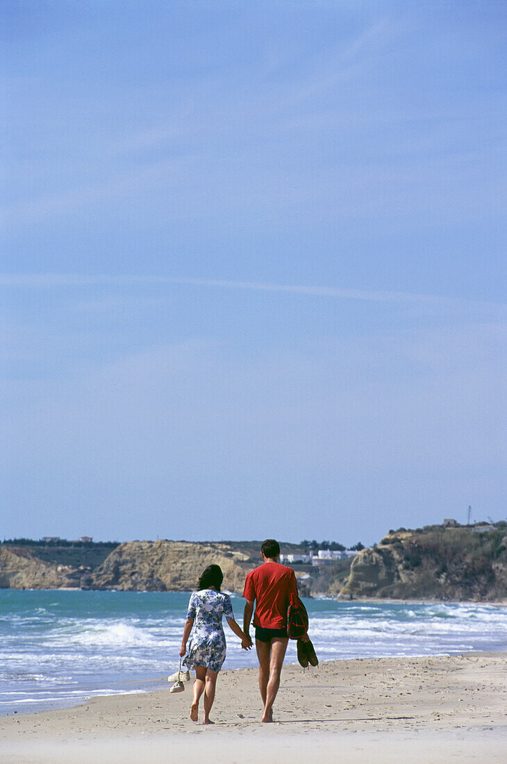 Couple Walking Hand In Hand Down The Beach