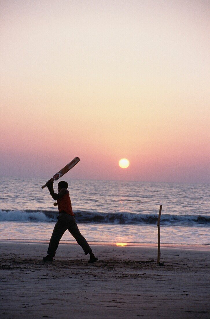 Mann spielt Kricket am Strand bei Sonnenuntergang