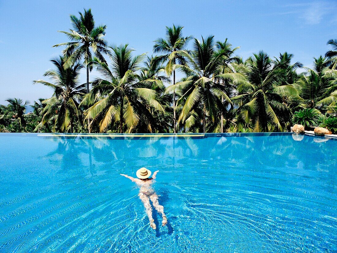 Frau schwimmt im Pool unter Palmen
