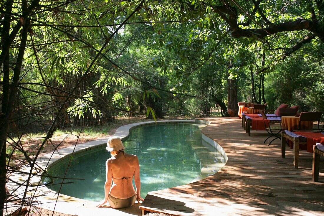 Frau sitzt am Rande eines Swimmingpools im Dschungel