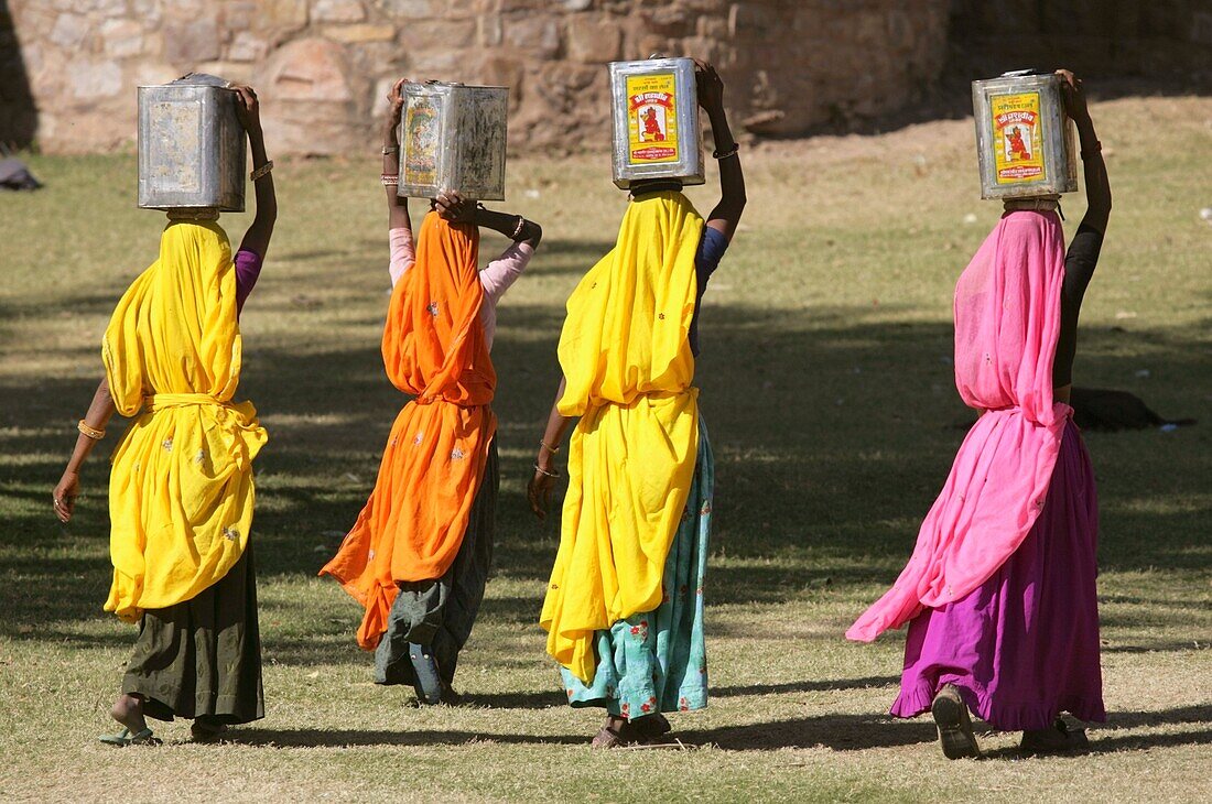 Frauen in bunten Saris tragen Metallkisten auf dem Kopf