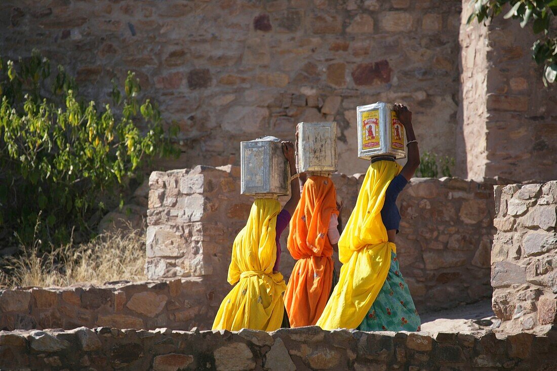 Drei Frauen in Saris, die Kisten auf dem Kopf tragen