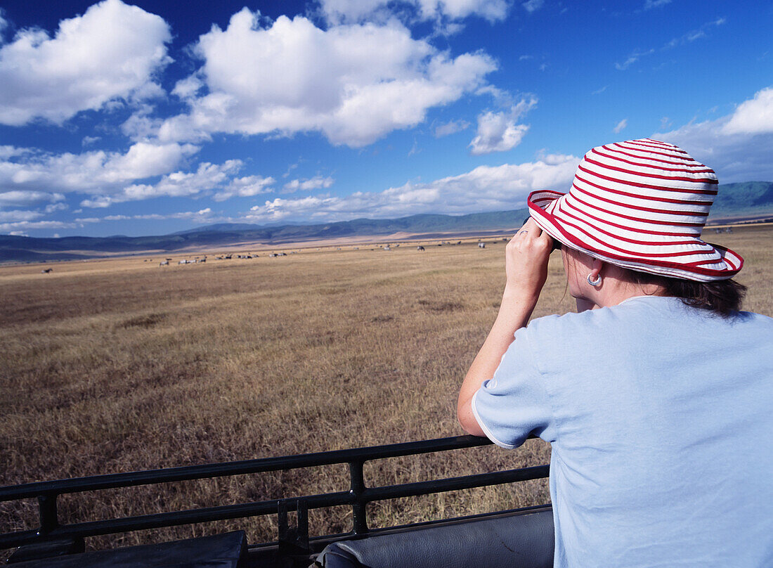 Woman Looking Through Binoculars At Animals In Ngorogoro National Park