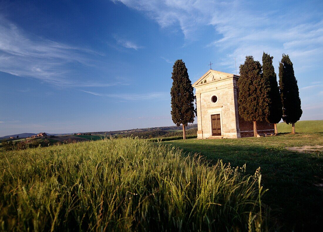 Zypressen neben einer kleinen Kapelle in der Abenddämmerung bei San Quirico D'orcia