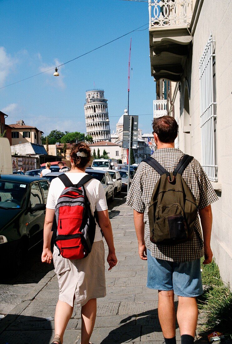 Tourists Walking Along Via Card. With Leaning Tower Of Pisa In The Distance