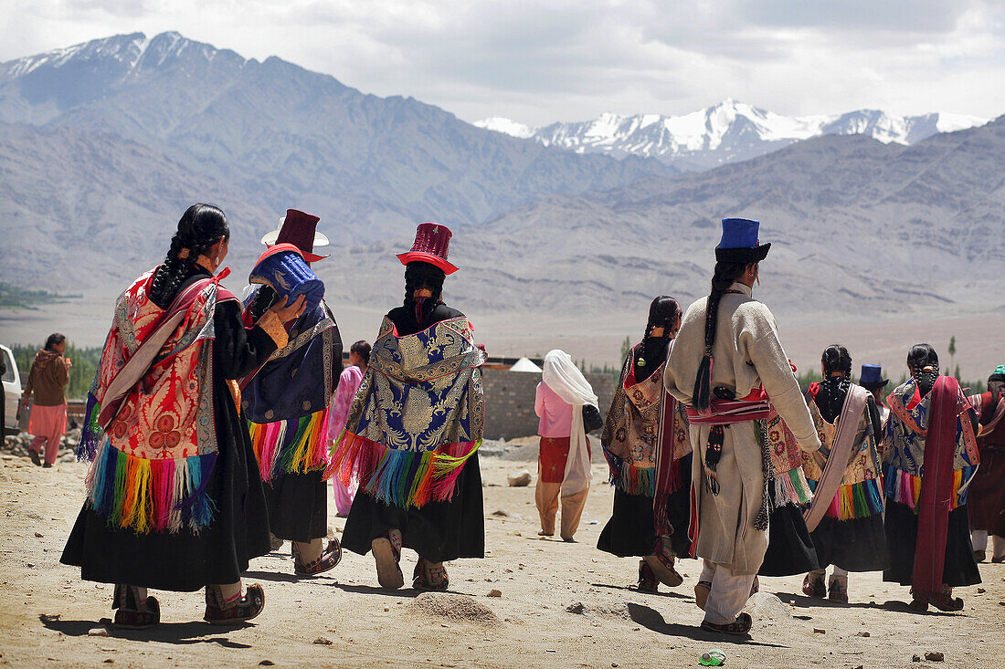 Menschen in traditioneller Kleidung und Hüten gehen unterhalb der Berge