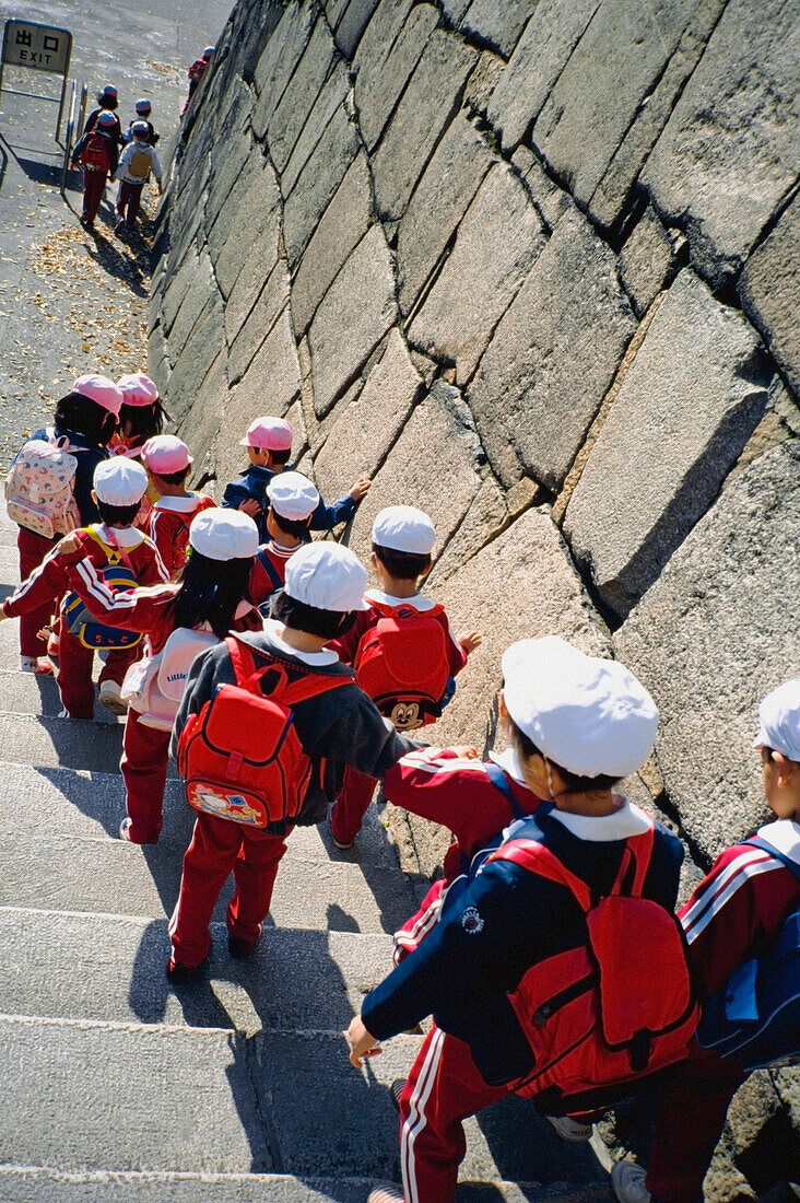 Schulkinder (6-7 Jahre) gehen die Steintreppe hinunter, Rückansicht, erhöhte Ansicht