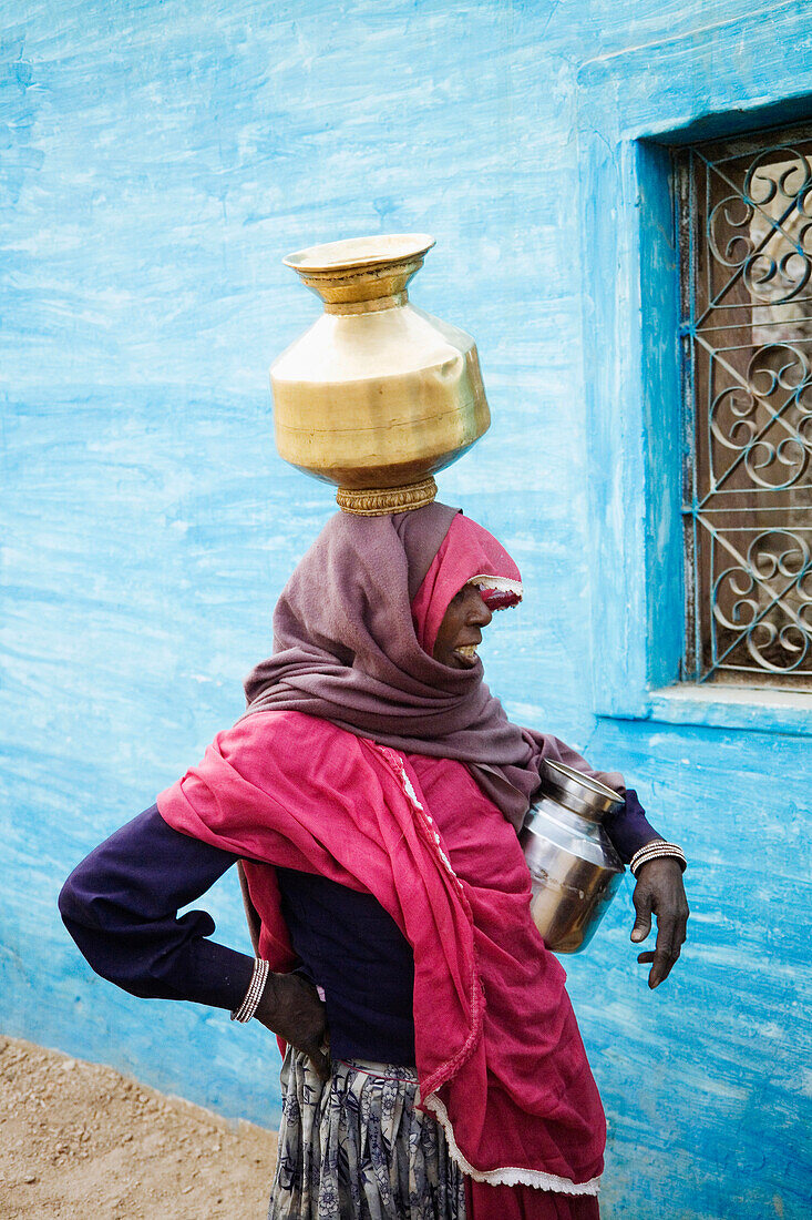 Frau in traditioneller Kleidung trägt einen Messingtopf auf dem Kopf