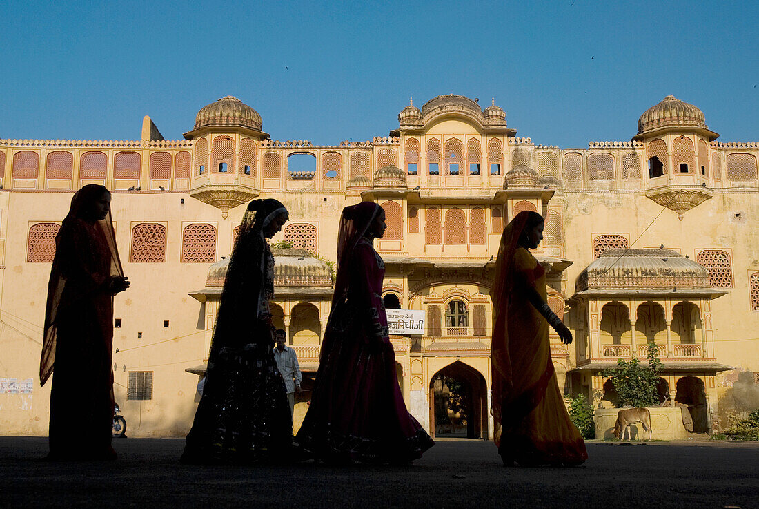 Silhouette Of Four Women In Saris Walking Past Old Building