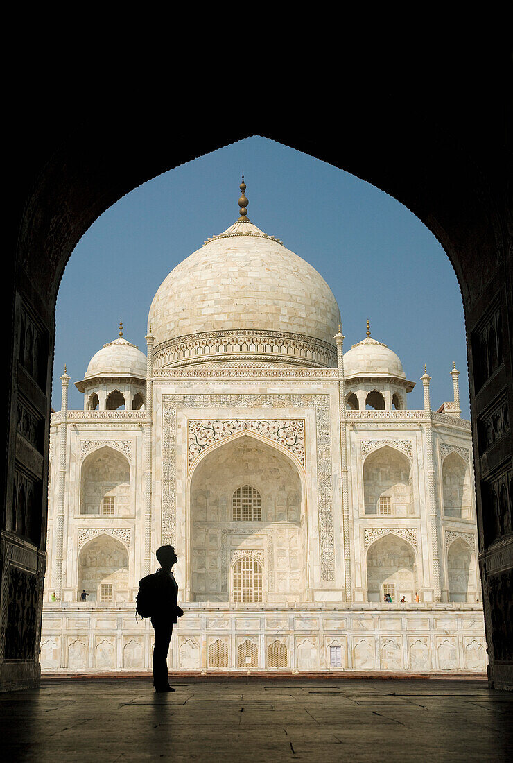 Silhouette einer Frau mit Rucksack in einem Torbogen, die das Taj Mahal bewundert