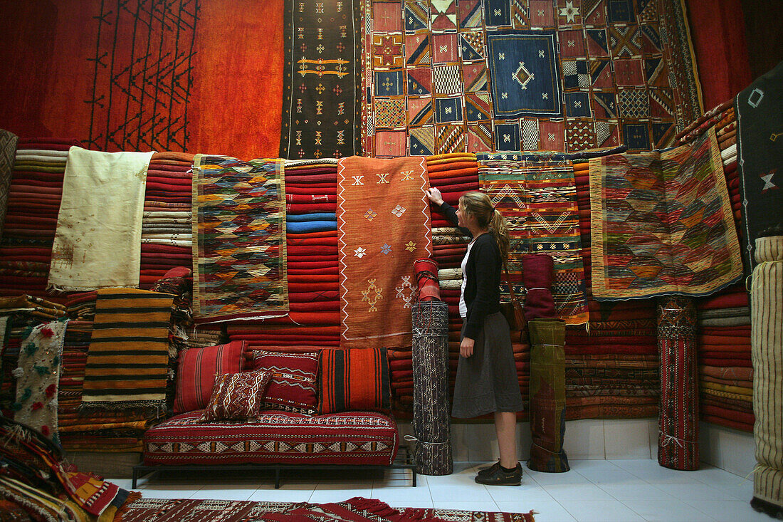 Young Woman Browsing For Moroccan Carpets And Rugs In A Market Stall In The Souk.