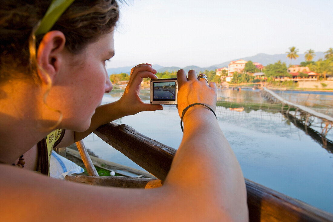 Junge Frau sitzt an einer Bar mit Blick auf den Nam Song Fluss.