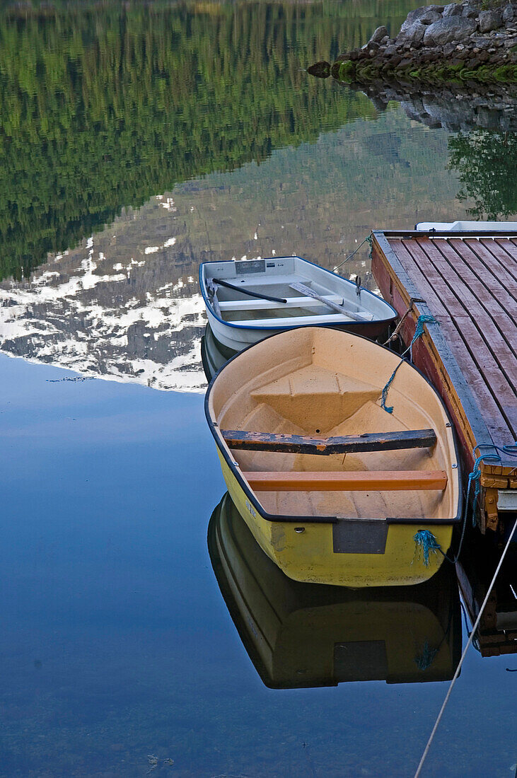 Kiefern und Berge spiegeln sich im See neben den Ruderbooten