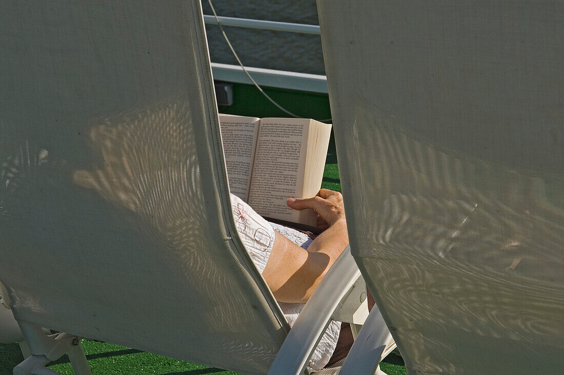 A Woman Relaxing In A Chair Reading A Book Onboard A River Cruise