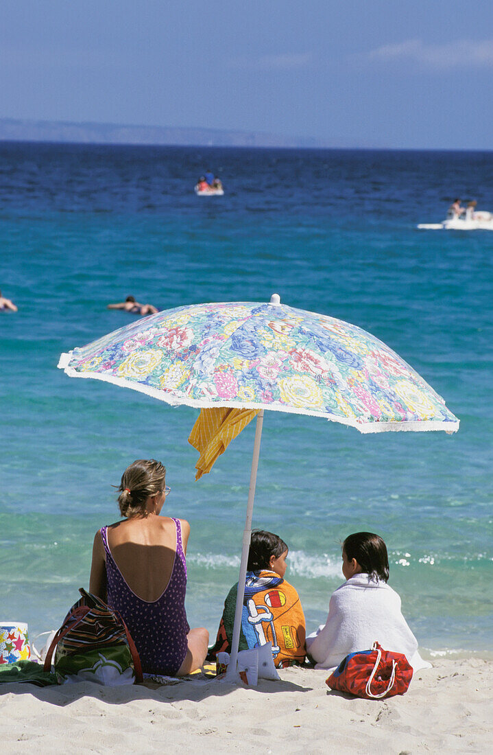 Mutter mit Töchtern unter einem Sonnenschirm am Strand